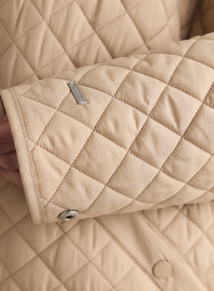 Beige quilted jacket sleeve detail showing the aim'n metal logo and buttoned cuff. [M-170cm]