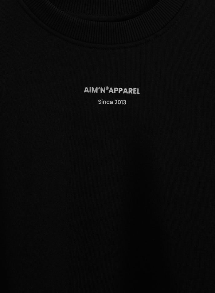 Silver aim'n logo print on a black terry sweatshirt with a ribbed round neckline.