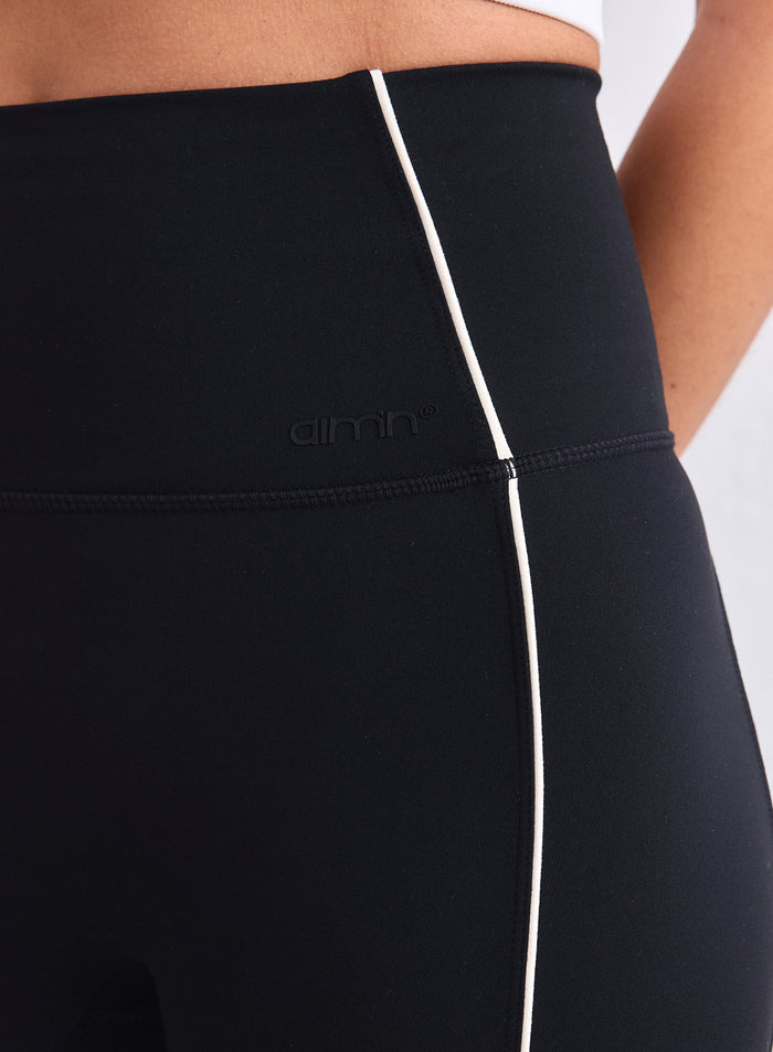 Close-up of high-waisted black Sense Contrast Tights featuring white piping and the aim'n logo. [XS-165cm]