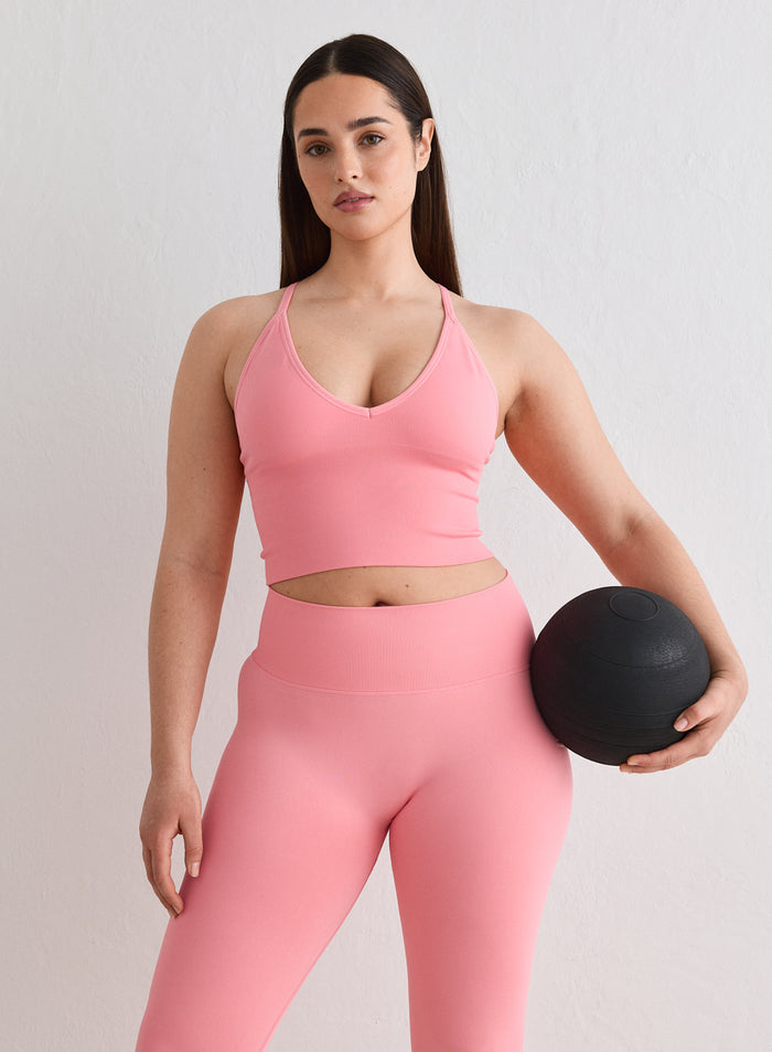 A woman wearing a Blush Shape Seamless Cross Back Bralette and matching leggings by aim'n, holding a black medicine ball [L-174cm]