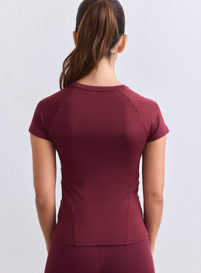 Back view of a woman wearing a merlot aim'n Soft Basic Short Sleeve training top in jersey. [S-165cm]