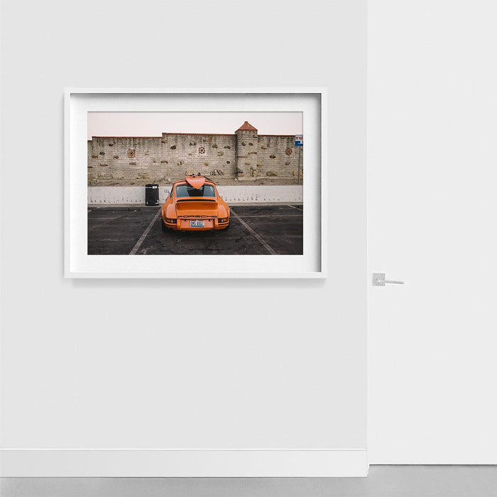 Framed photograph of an orange Porsche 911 Carrera 2 7 RS with a surfboard on top in a white frame