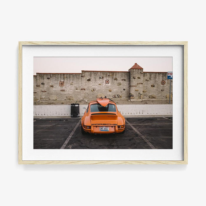 Framed photograph of an orange Porsche 911 Carrera 2 7 RS with a surfboard on top in a light wooden frame