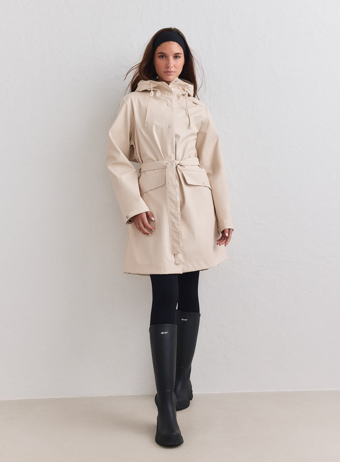 Sand waterproof rain jacket features a belted waist and hood, styled with black boots by aim'n. [M-178cm]