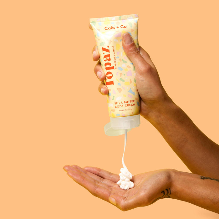 Person squeezing topaz body cream onto their hand against an orange background