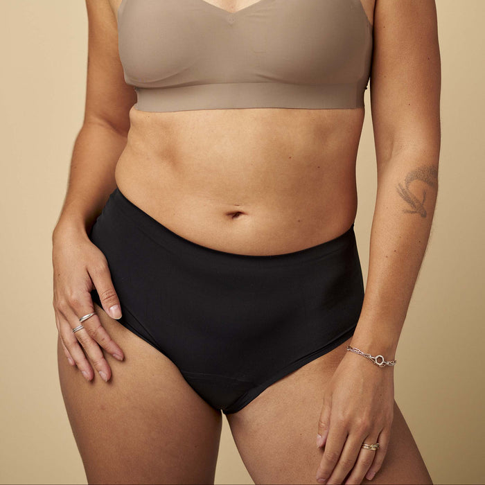 Woman wearing a beige bralette and black high-waisted shorts on a beige background