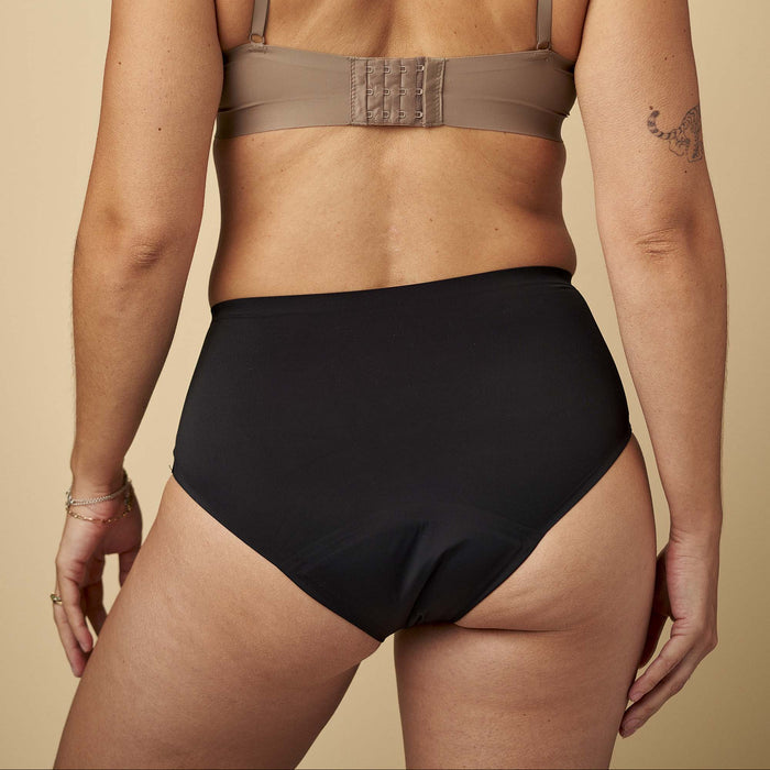 Person wearing a beige bra and black high-waisted underwear on a beige background