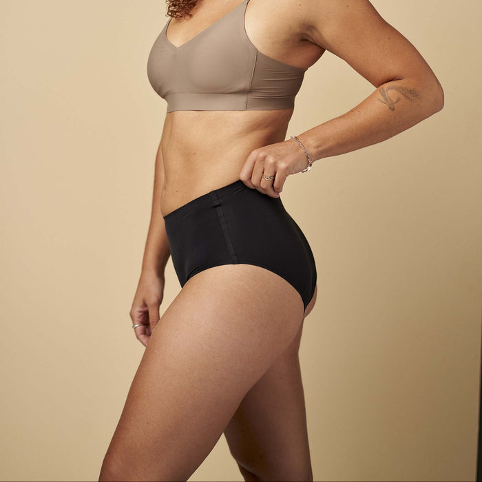 Woman wearing a beige sports bra and black shorts on a beige background