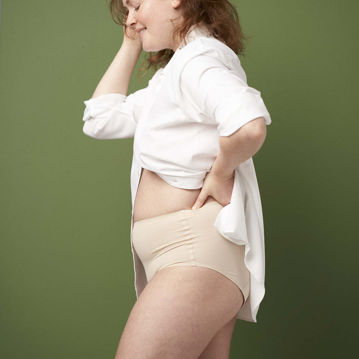 Woman wearing a white shirt and beige underwear against a green background