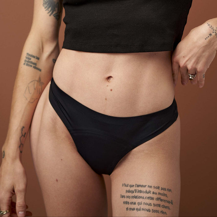 Person wearing a black crop top and black underwear against a brown background