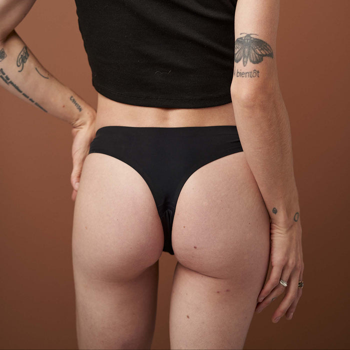 Person wearing a black crop top and black underwear against a brown background
