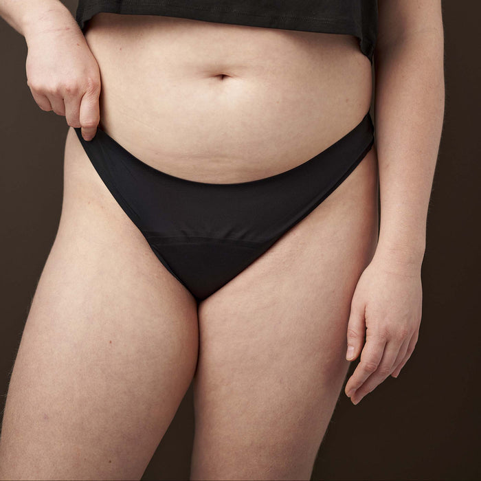 Person wearing a black crop top and black underwear against a brown background