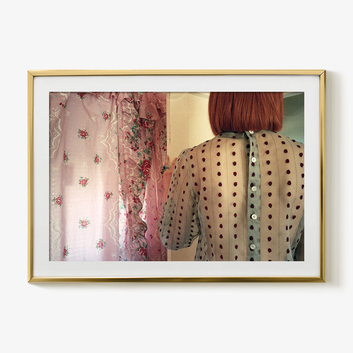 Framed photograph of the back of a person with short red hair wearing a sheer polka-dot top with button closure