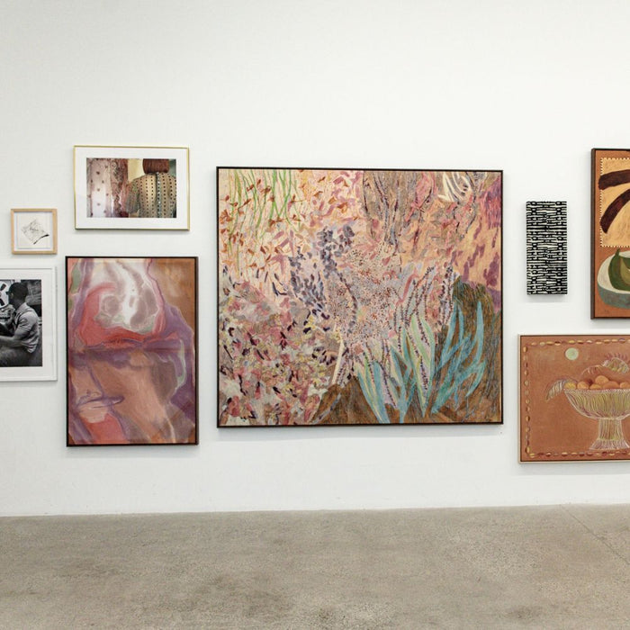 A collection of diverse paintings on a white gallery wall including abstract landscape and portrait pieces