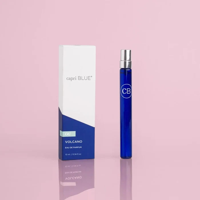 A blue and white spray pen bottle of Capri Blue Volcano Eau De Parfum, with the brand's logo on the cap, displayed next to its white box packaging with the product name and scent noted.