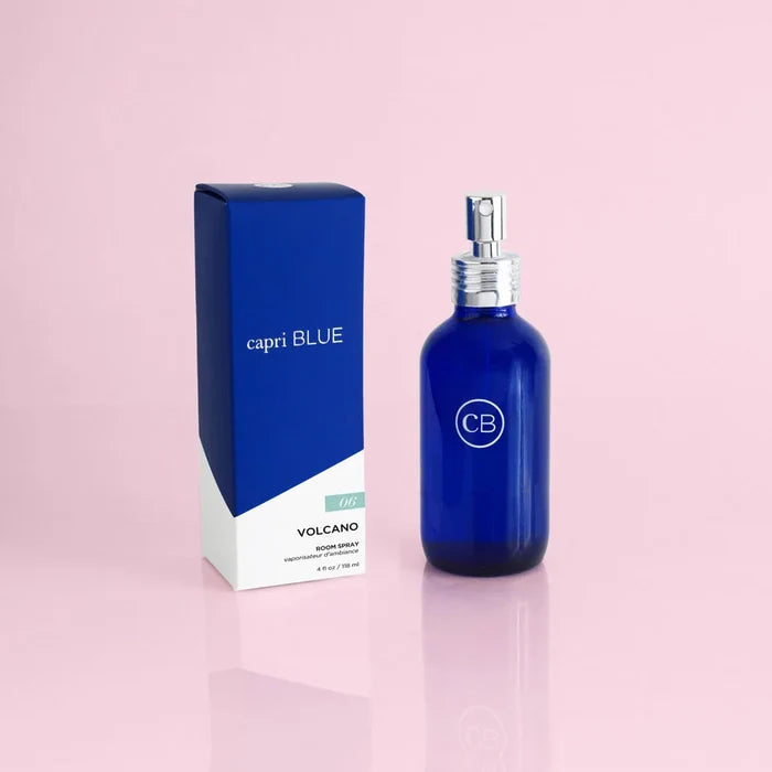 A blue bottle of 'Volcano Signature Room Spray' with a white spray nozzle, next to its blue packaging box, placed on a pink background.